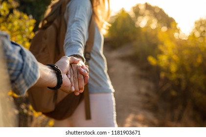 Close-up shot of young couple on a hiking trip. Cropped image of young man and woman hikers holding hands while walking on mountain trail.