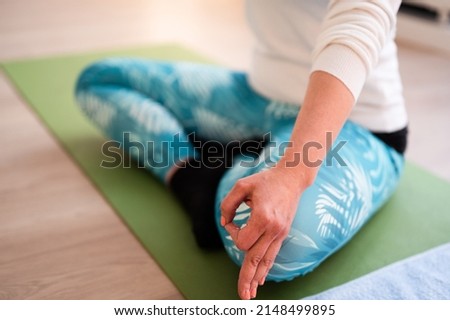 Close-up shot of young female's hand holding fingers in Gyan mudra as symbol of wisdom. Caucasian woman in active wear practice yoga while sitting on green exercise mat  in lotus pose.  Stock fotó © 