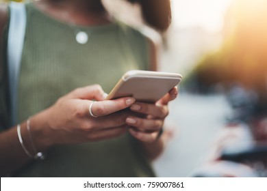 Closeup shot of young hipster girl chatting with family at social networks, sunlight on the background, womanâ??s hands using smartphone outdoor, lifestyle and communication concept