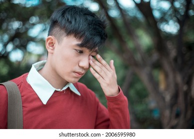 Closeup shot of a young man with irritated eyes or wiping tears from his face. Smart casual wear. Outdoor scene.