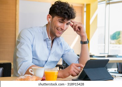 Closeup shot of young man smiling and using digitaltablet at cafÃ?Â?Ã?Â©. Guy is doing breakfast and in the meantime making a video call with tablet and headphone. Happy man using palmtop during breakfast. 