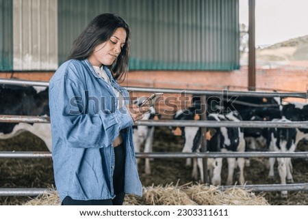 Close-up shot of a young woman farmer consulting and writing tasks on her mobile phone with a serious gesture next to her cows.