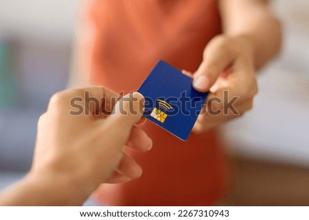 Closeup shot of young woman giving blue credit card to female hand, pov of unrecognizable lady passing bank card to client, offering financial services or paying for shopping, selective focus