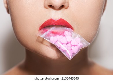 Closeup Shot Of A Young Woman Holding A Transparent Ziplock Bag Filled With Pink Heart Shaped Pills In Her Mouth.
