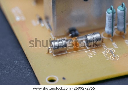A close-up showcases various electronic components on a printed circuit board. Visible are a fuse, resistors, and other elements which are part of a modern electronic device.