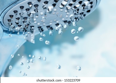 Closeup of a shower head with sprinkling water, blue toned photo.