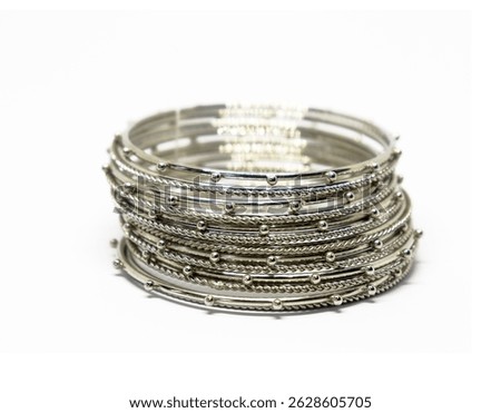 Close-up shows a layered stack of shiny, silver-toned bangles featuring both smooth and twisted metal designs, adorned with small, metallic beads. Isolated on white.