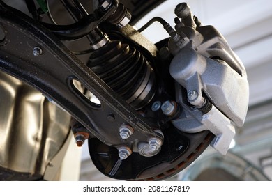 Close-up shows the suspension arm of a modern car in place of the connection with a ball joint and a brake caliper. Selected focus. Car service and auto parts.