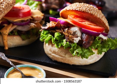 Close-up shredded bbq chicken sandwiches with cheddar cheese, tomatoes, red onions, lettuce with original burger sauce: classic mayonnaise and sriracha on a black slate
