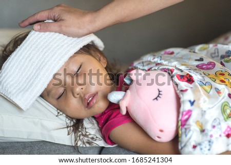 Closeup of sick little baby girl with fever sleeping in bed. Mothers hand caring for her. 