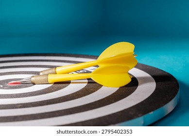 A close-up side angle shot of two yellow darts resting on top of a black and white circular dartboard, representing strategic pauses, planning, preparation, and project objectives.