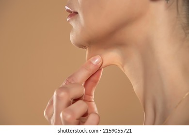 A close-up and side profile view of a caucasian lady pinching the loose skin at the front of her throat. Commonly called a turkey neck and corrected with a platysmaplasty. - Shutterstock ID 2159055721