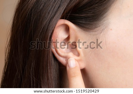 A closeup and side profile view of a hard of hearing girl, using finger to point towards the ear, hand gesture of disabled girl struggling to hear conversation.