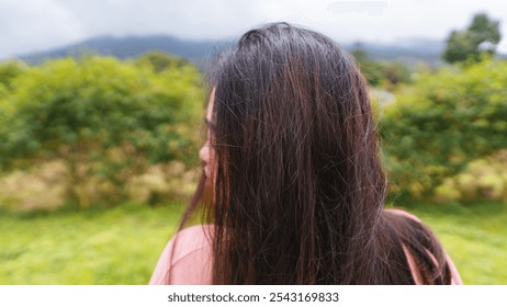 A close-up side profile of a young woman with long, dark hair as she stands in a natural outdoor setting - Powered by Shutterstock