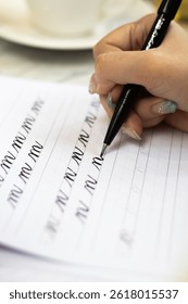 A close-up side shot of a hand practicing modern calligraphy with a black pen on a guide sheet. detailed strokes, precise repetition, and a focus on developing pen control skills. 