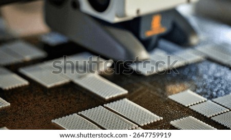 A close-up side view of a 3D printer nozzle actively printing small rectangular calibration grids in white filament on a textured heated bed, capturing the intricate surface texture and precise patter