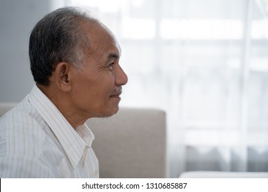closeup from side view of Asian old man sitting on the sofa a background of window with curtain