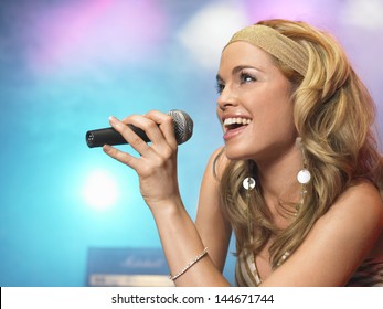 Closeup side view of a beautiful young woman singing into microphone on stage at concert