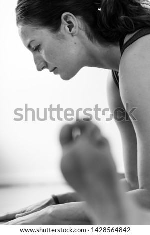 Close-up side view of a brunette woman in her 30’s practicing yoga at home, doing a wide legged seated forward bend asana. Vertical format.