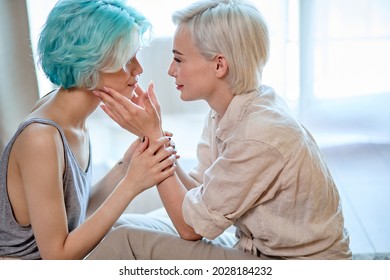 Close-up Side View Of Caucasian Ladies Lesbian Couple Talking About Love, Touching Each Other While Sitting On Floor At Home In Living Room, Window In The Background. Two Short-haired Women In Love