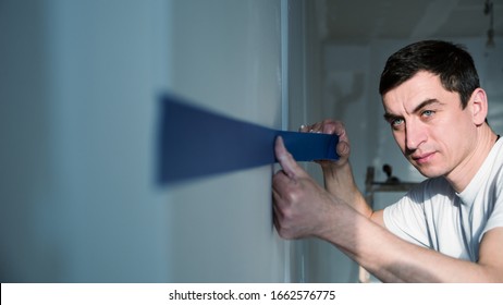 Closeup Side View Of Early 30's Man Taping A Drywall With A Piece Of Duck Tape