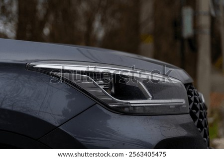 Close-up side view or elegant headlight of modern black coloured car covered with some rain drops of water outdoors on autumn or spring city street. Soft focus. Copy space. Automobile details theme.