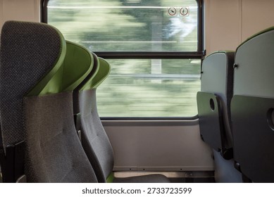 A close-up side view of empty gray and green fabric passenger seats inside a clean, modern commuter train or tram next to a large window during the day.