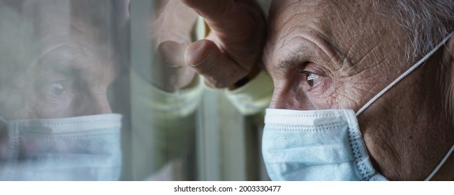 Closeup side view large scale portrait of sick male patient wearing face mask and looking through window glass of hospital - Powered by Shutterstock