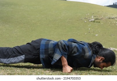 Close-up side view of a long haired Indian young guy doing fist push ups in the nature