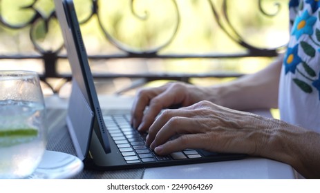 Closeup side view of mature old womans hands using a laptop tablet computer with a drink on a table at cafe in europe. Traveling digital nomad concept. - Powered by Shutterstock