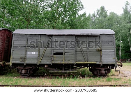 A close-up side view of an old weathered wooden cargo boxcar with painted numbers standing on rails in a grassy area.