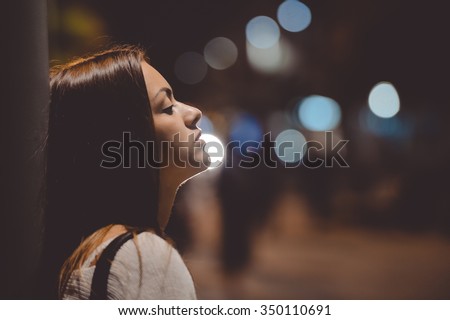 Closeup side view portrait of young sad thoughtful woman leaning against street lamp at night on bokeh copy space background