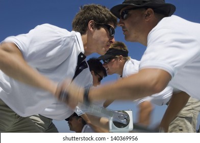 Closeup side view of sailors operating windlass on yacht against clear blue sky