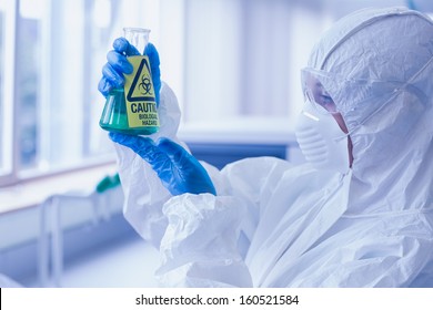 Close-up side view of a scientist in protective suit looking at hazardous blue chemical in flask at the laboratory