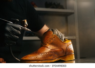 Close-up side view of unrecognizable shoemaker wearing black gloves spraying paint of light brown leather shoes. Concept of cobbler artisan repairing and restoration work in shoe repair shop. - Powered by Shutterstock