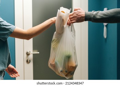 Close-up Side View Of Unrecognizable Young Woman Customer Receiving Groceries Bag With Healthy Food From Delivery Man On Doorstep At Apartment. Courier Male Delivering Food Meal To Client At Home.