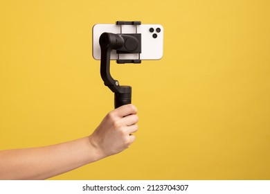 Closeup Side View Of Woman Hand Holding Steadicam With Phone, For Making Video Or Has Livestream. Indoor Studio Shot Isolated On Yellow Background.