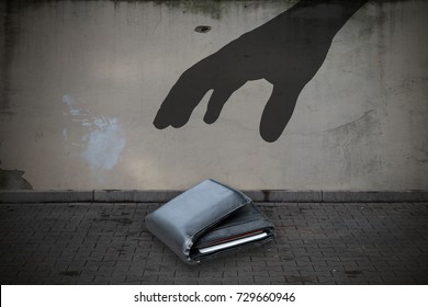 Close-up Of Silhouette Hand Picking Up Fallen Wallet On Street