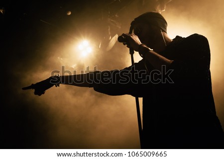 Close-up silhouette of a singer on the stage. Smoke and yellow stage lights in the background.