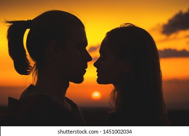 Close-up Of The Silhouettes Of A Young Millenial Couple In Love With A Man And Girl Against The Sunset Golden Sky. They Look At Each Other. Young Family