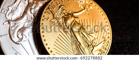 closeup of silver eagle and golden american eagle one ounce coins on black background