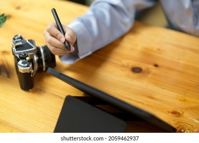 Close-up simple wooden worktable with camera, tablet computer and woman's hand holding stylus pen.