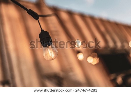Close-up of a single hanging string light with a blurred background of warm tones at dusk.