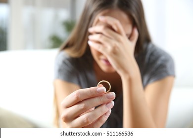Closeup of a single sad wife after divorce lamenting holding the wedding ring in a house interior