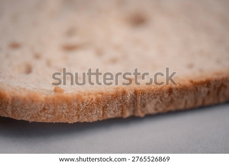 Close-up of a single slice of bread. Soft, porous texture with tiny air holes. Golden-brown crust edges show slight crispness. Ideal for food blogs or breakfast concepts