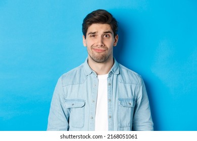 Close-up Of Skeptical And Awkward Guy Smirking, Feeling Uncomfortable, Standing Over Blue Background