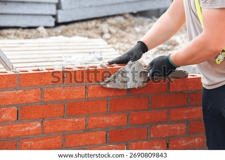 Close-up of skilled bricklayer working on construction site laying red bricks for wall construction