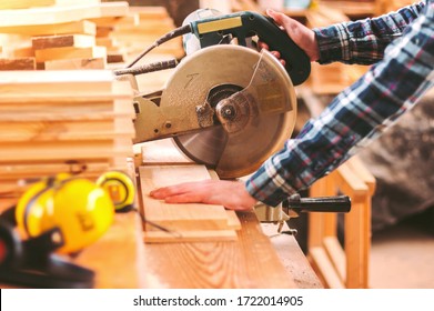 Closeup skilled cabinet maker cutting wood board with electric circular saw at woodworking sawmill. Professional cabinet maker use circular saw at sawmill factory. Wooden furniture production. Joinery