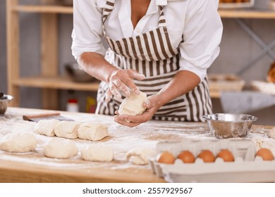 Close-up of skilled female baker hands working with small dough pieces on flour-dusted wooden table, preparing for baking in artisan bakery - Powered by Shutterstock