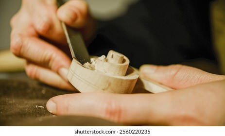 Close-up of skilled luthier's hands meticulously shaping a violin scroll using a chisel, demonstrating the artistry and precision involved in crafting string instruments - Powered by Shutterstock